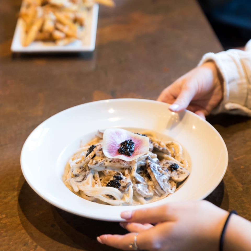 Truffle pasta with mushrooms, caviar, and an edible flower being served at the table.