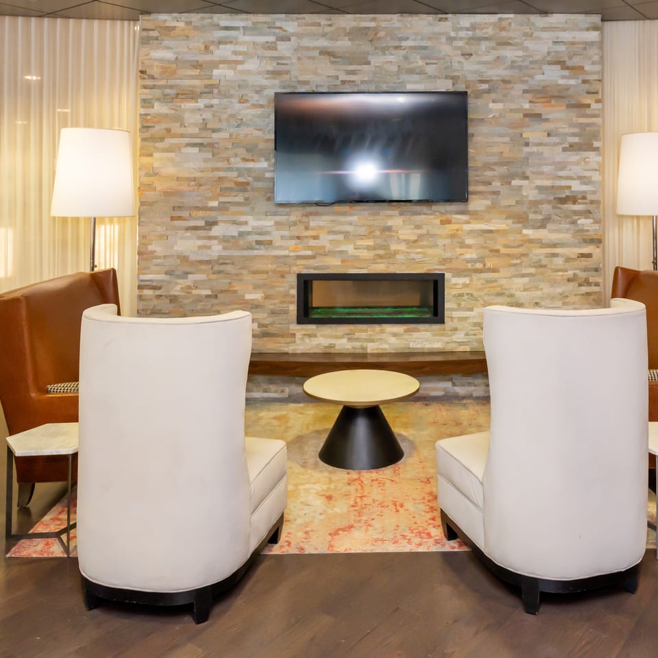 Lounge area with two white chairs, two brown chairs, a fireplace, and a TV on a stone wall.