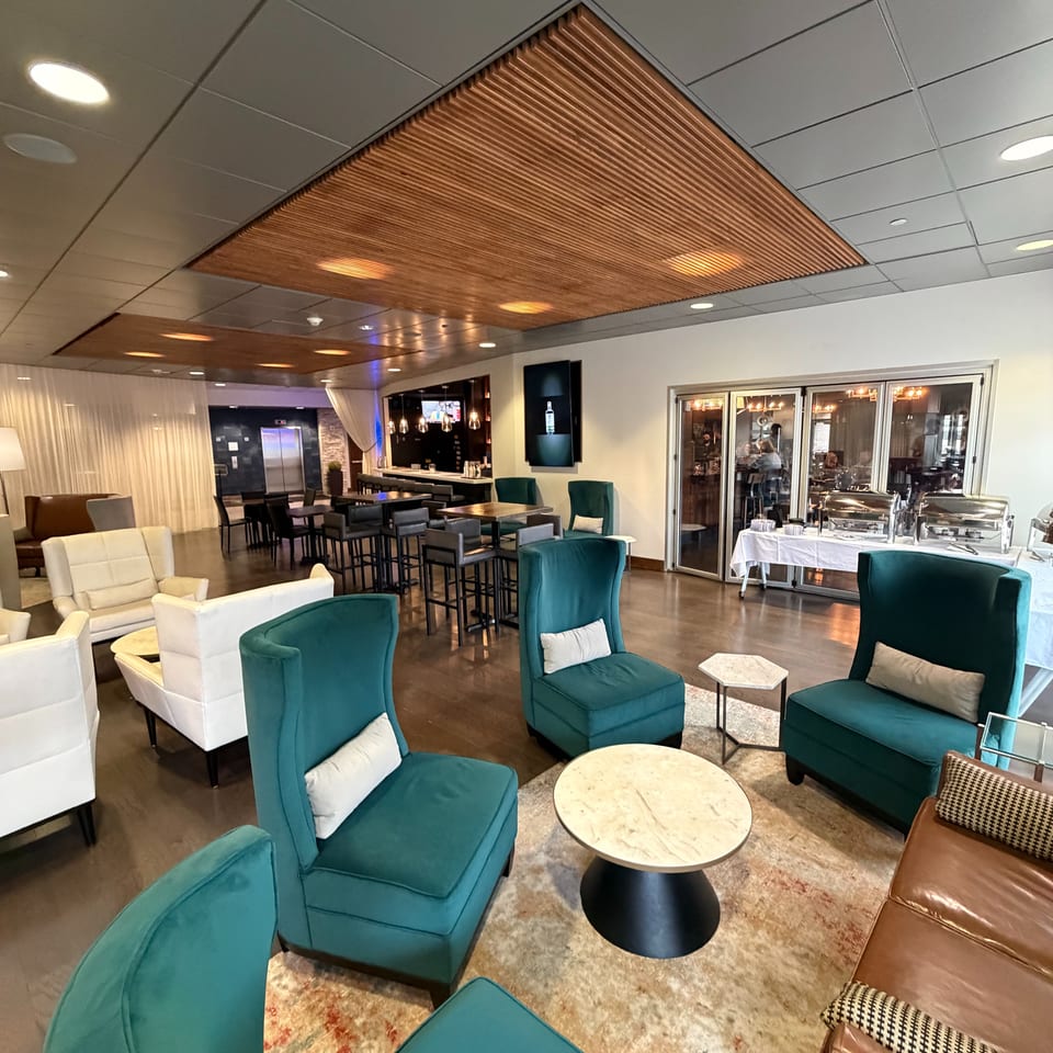Elegant restaurant lounge with teal and white seating, marble tables, wood ceiling accents, bar, and buffet service.