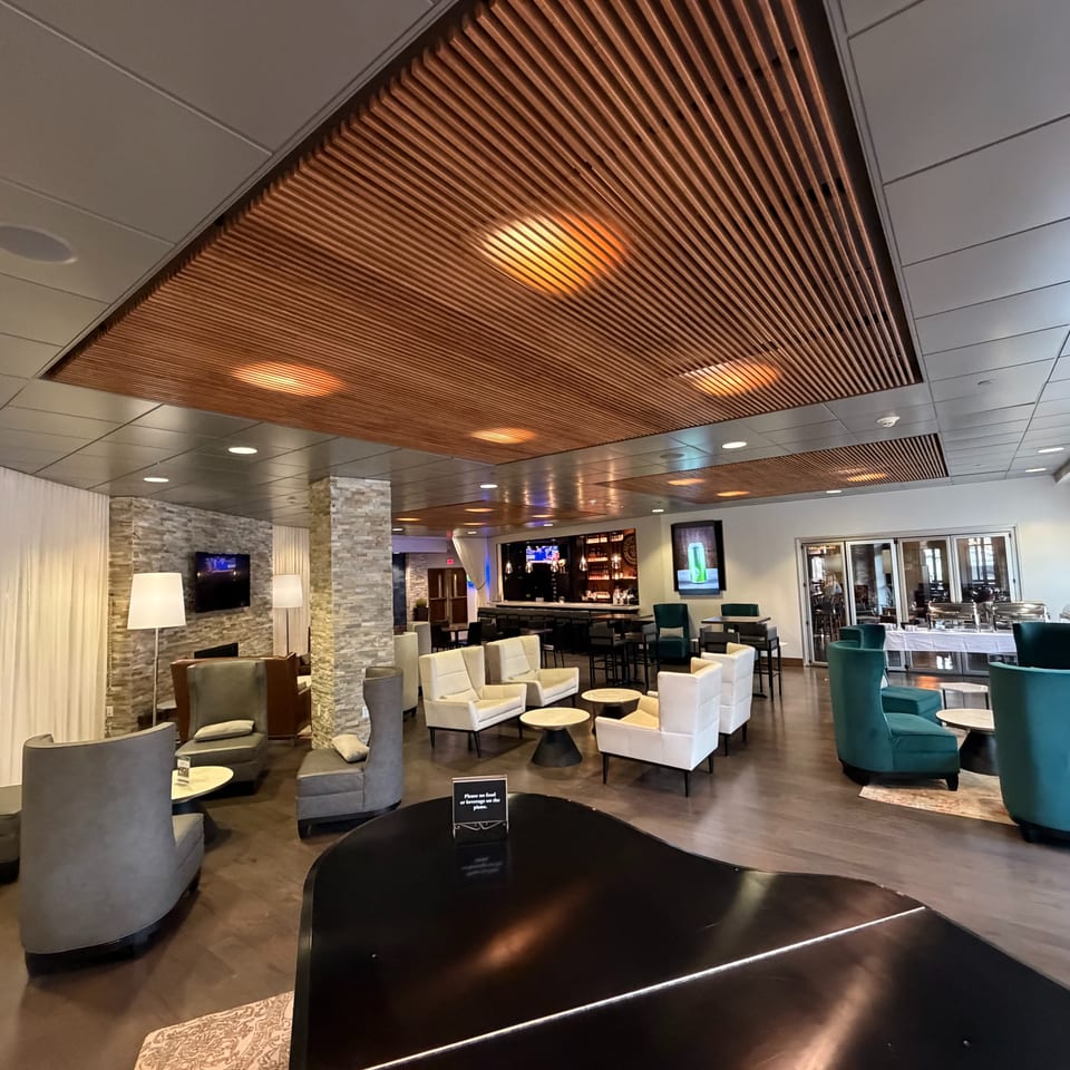Modern restaurant lounge with upholstered seating, stone columns, a bar, buffet area, and decorative wooden ceiling panels.