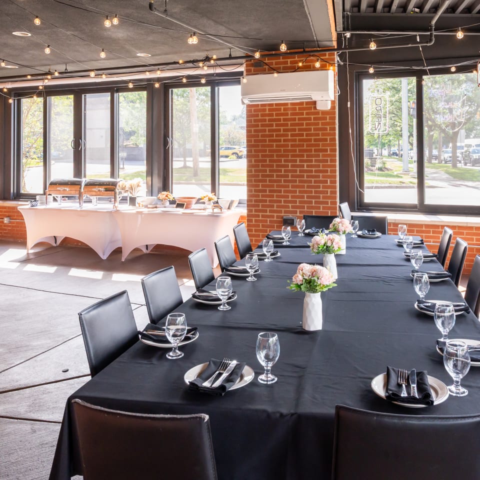 Elegant restaurant dining room with black tablecloths, place settings, floral centerpieces, buffet station, brick walls, and string lights.