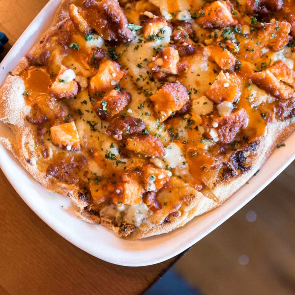 Buffalo chicken flatbread topped with blue cheese and herbs, close up.