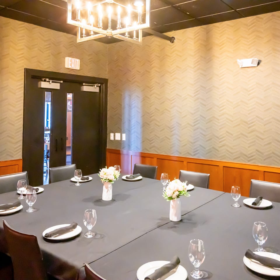 Elegant private dining room with set tables, white floral centerpieces, dark linens, and warm geometric lighting.