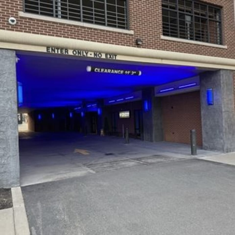 Blue-lit restaurant parking garage entrance beneath a brick building, marked with clearance and enter-only signage.