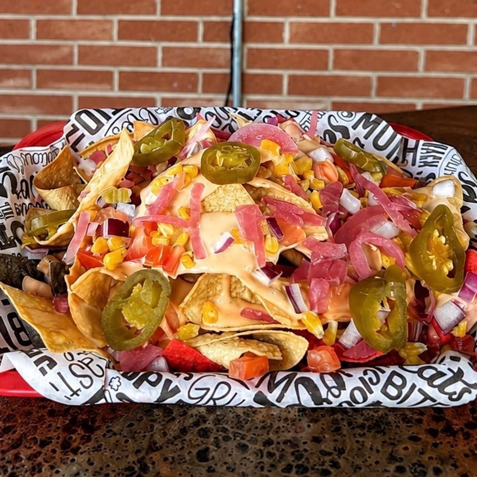 Loaded nachos topped with jalapeños, pickled onions, corn, tomatoes, red onions, and melted cheese on a restaurant table.