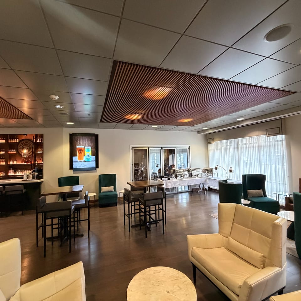 Elegant restaurant lounge with bar, green chairs, cream sofas, dining tables, buffet station, and large windows.