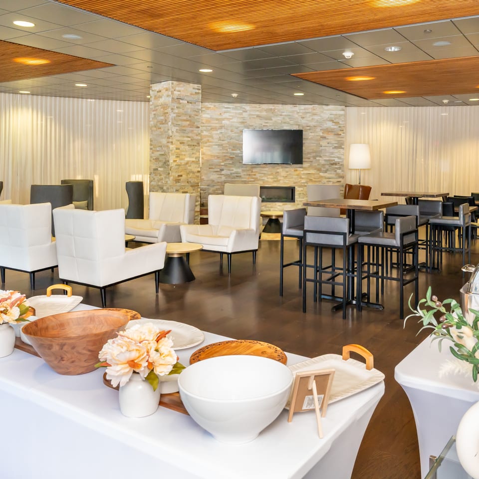 A modern lounge area with white and gray seating, high-top tables, and a buffet spread.