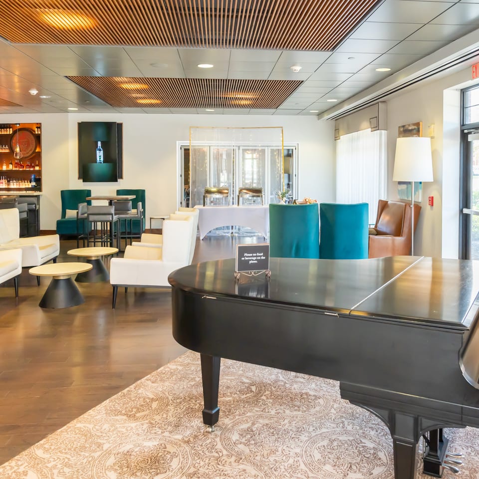 A spacious lounge area with a grand piano, bar, and various seating arrangements.