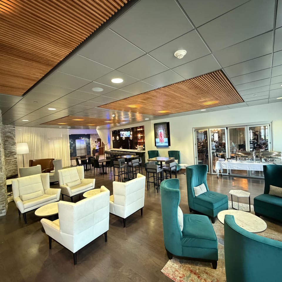 Spacious restaurant lounge with teal and cream seating, dining tables, stone accents, a bar, and buffet service beneath a wood-paneled ceiling.