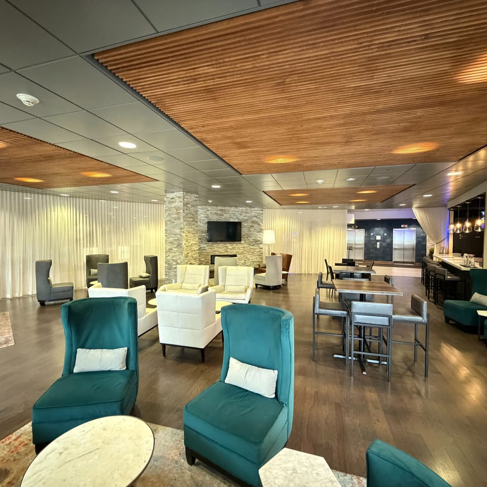 Contemporary restaurant lounge with teal and cream seating, wood tables, pendant lights, draped walls, and a stone television feature wall.